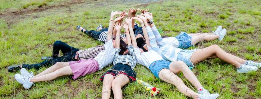 group of friends in a circle laying on grass with hands outstretched to heaven