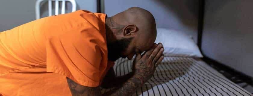 man in prison wearing orange kneeling and bowing in prayer
