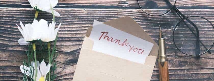 thank you note inside an envelope with glasses and pen on a table