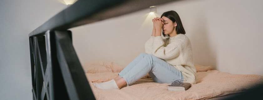 young woman praying while sitting on top bunk bed